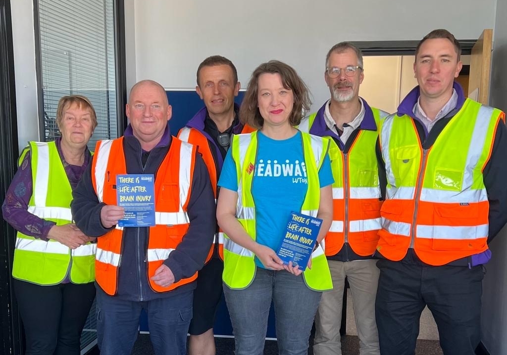 Two members of staff from Headway Luton meet with the team from Gist to collect a cheque and have a tour of the facilities. They are standing looking at the camera with hig vis vests on.