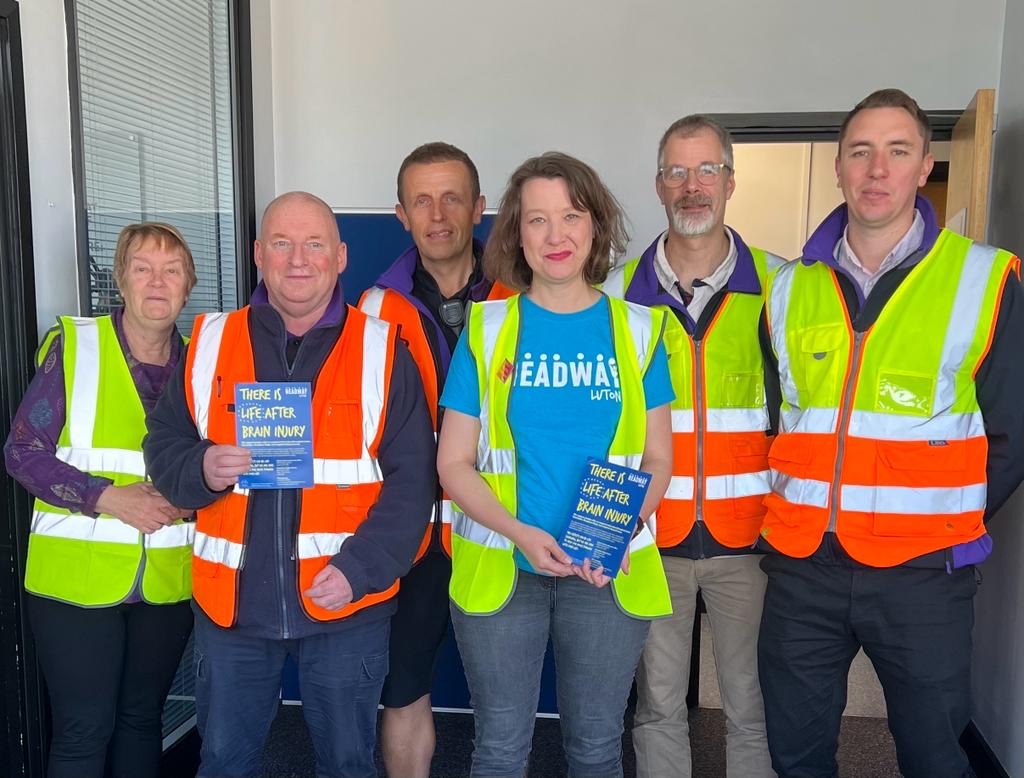 Two members of staff from Headway Luton meet with the team from Gist to collect a cheque and have a tour of the facilities. They are standing looking at the camera with hig vis vests on.