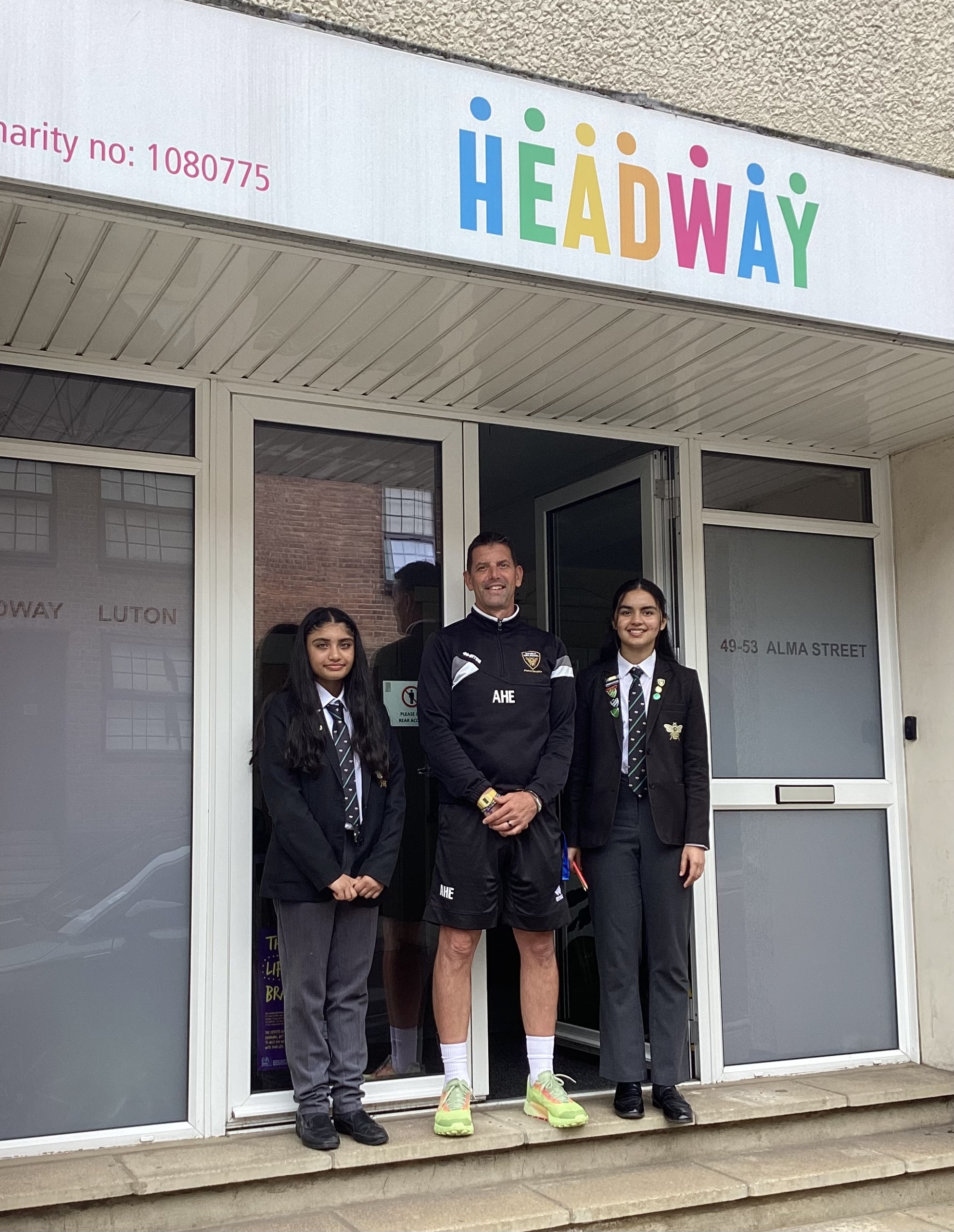 Mr Hince, Amara and Momina standing outside our front door underneath the Headway Luton logo.