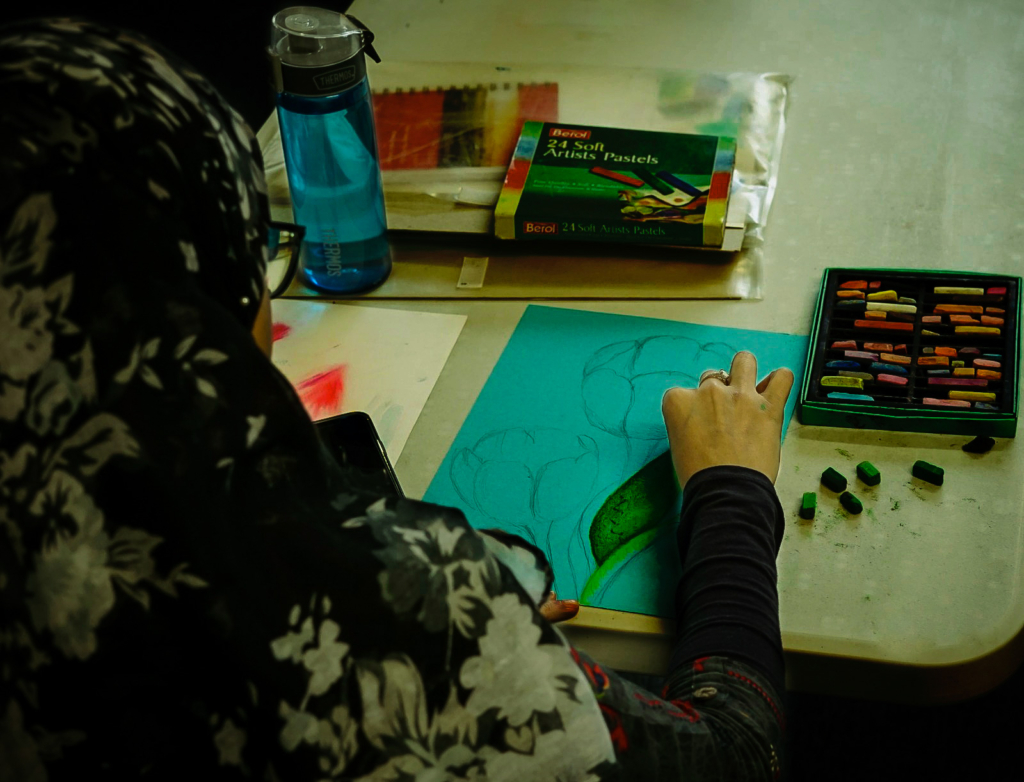 A photo of Millie drawing a flower using pastels. 