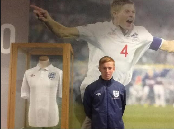 Freddie in an England football shirt standing next to a display box of a white England shirt worn by a player.