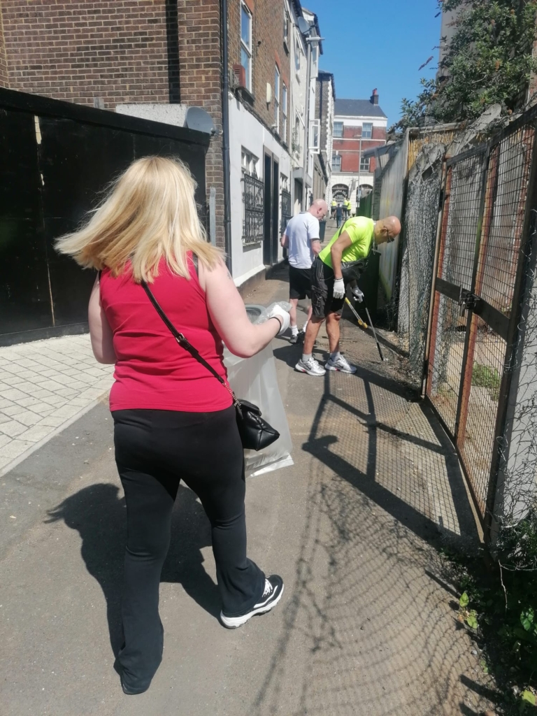 A woman with blond hair is litter picking in an alley way with others in Luton.