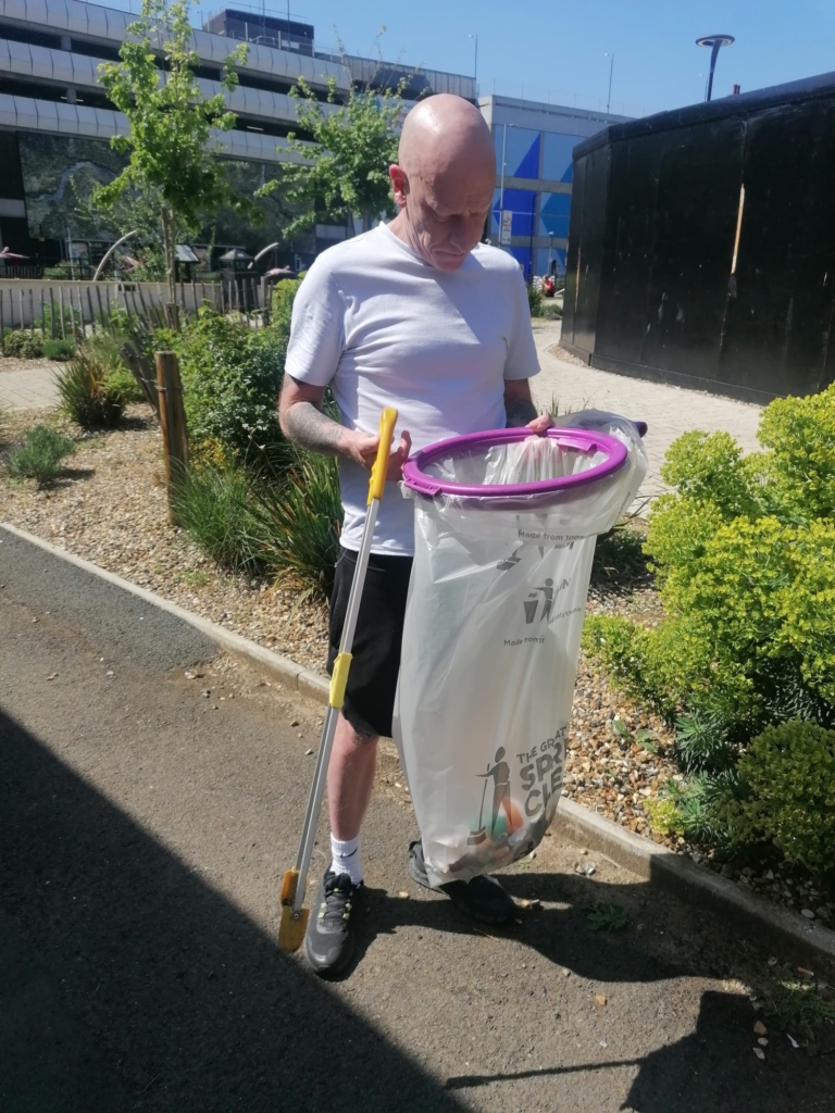 A white man with a bald head is looking inside the plastic bag where he has collected a range of litter types.