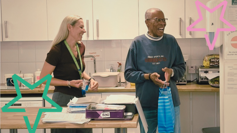 Kim, a white woman in her 40s with blond hair, presents Andrew,a black man in his 80s with a goodie bag of sweets and chocolate. They are both laughing.