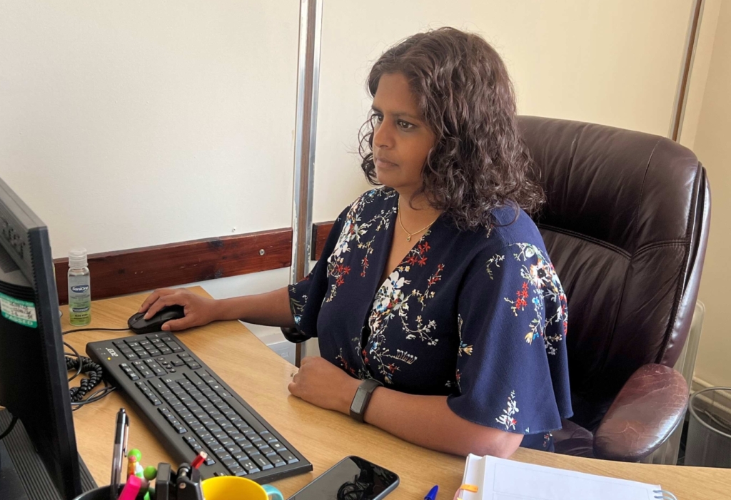 Kamini at her desk looking serious as she works on her computer.
