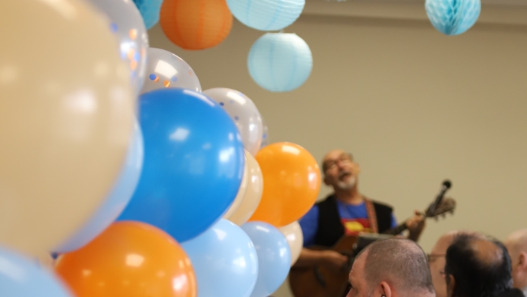 A man playing the guitar and singing surrounded by blue and orange balloons.